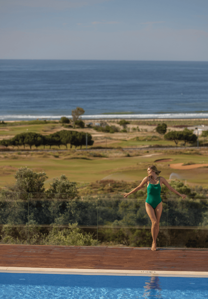 Mulher desfruta de piscina infinita com vista deslumbrante para o mar e campo de golfe no Palmares Resort, Algarve.