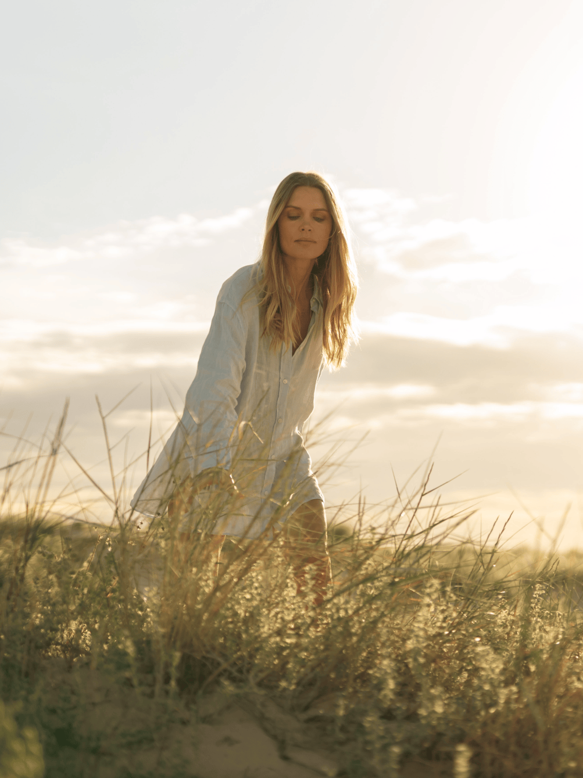 Mulher entre as dunas ao pôr do sol nas imediações do Palmares Living — momento sereno que celebra o contacto com a natureza e a luz única do Algarve.