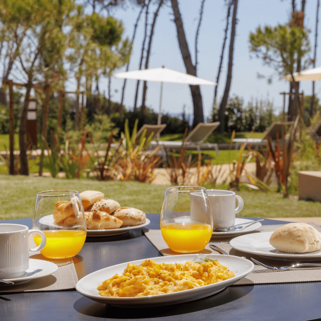 Pequeno-almoço servido ao ar livre com sumo de laranja e ovos mexidos, rodeado por natureza no Palmares Signature Apartments.