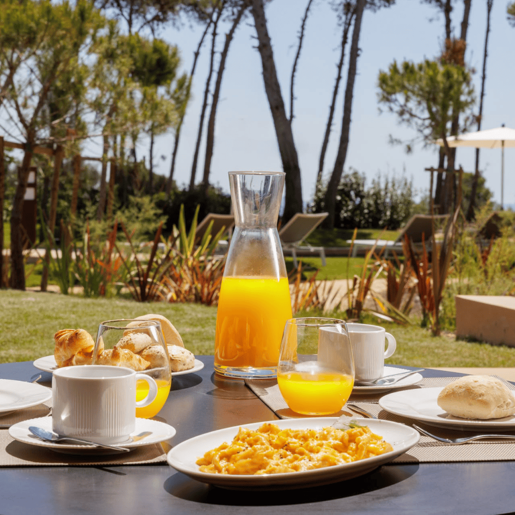 Mesa de pequeno-almoço com jarro de sumo de laranja natural no jardim do Palmares Signature Apartments.