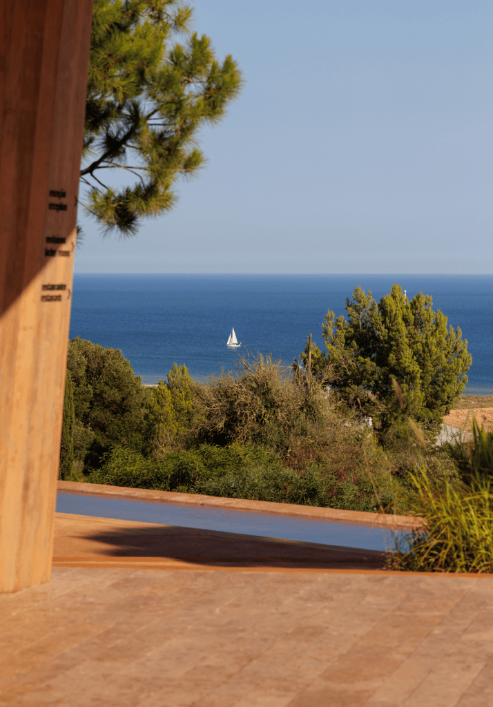 Vista para o mar a partir do Palmares, com barco à vela ao fundo e paisagem natural envolvente, simbolizando tranquilidade e exclusividade no Algarve.